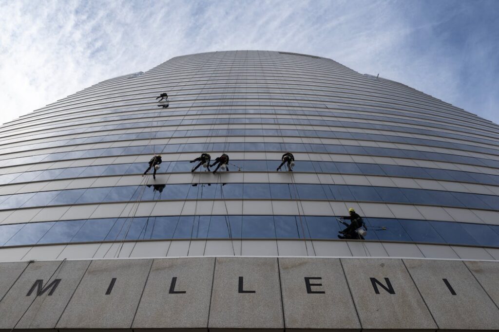 pexels photo 33163222 Window cleaners suspended high up a Santiago skyscraper against a vibrant sky.